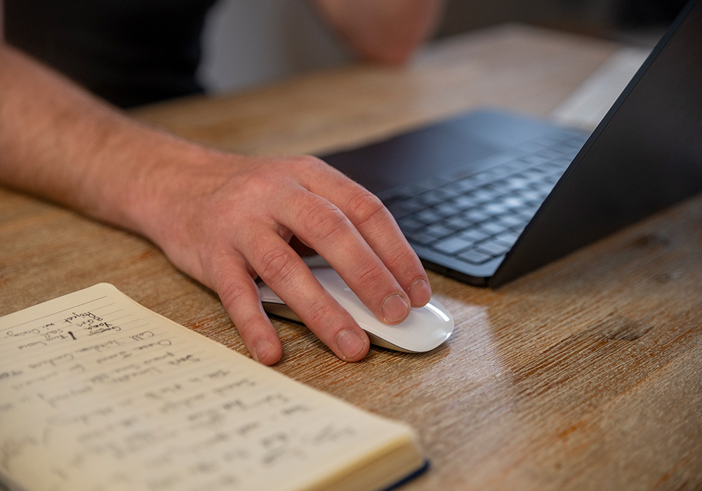close up of man's hand on a mouse with notepad beside him