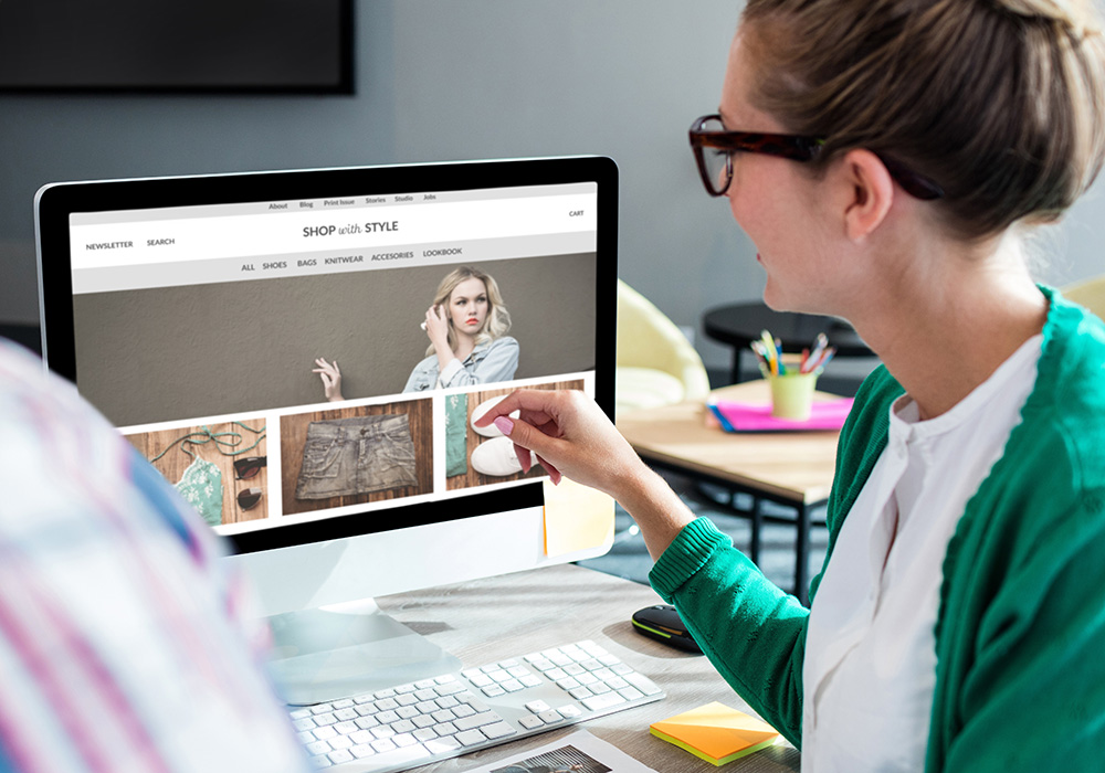 woman wearing glasses pointing to computer screen with a clothes website open