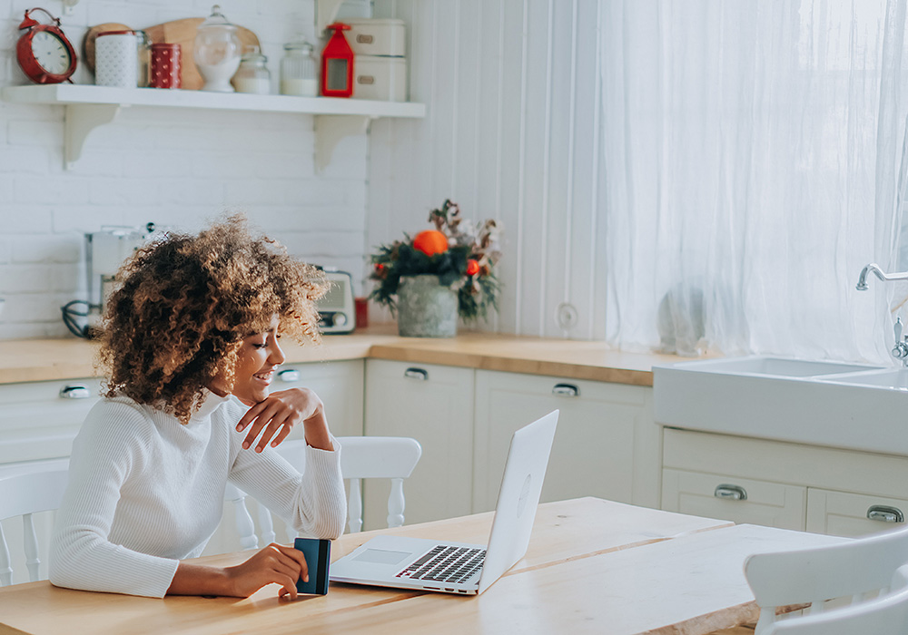 woman at kitchen table holding bank card on her laptop ready to make online purchase