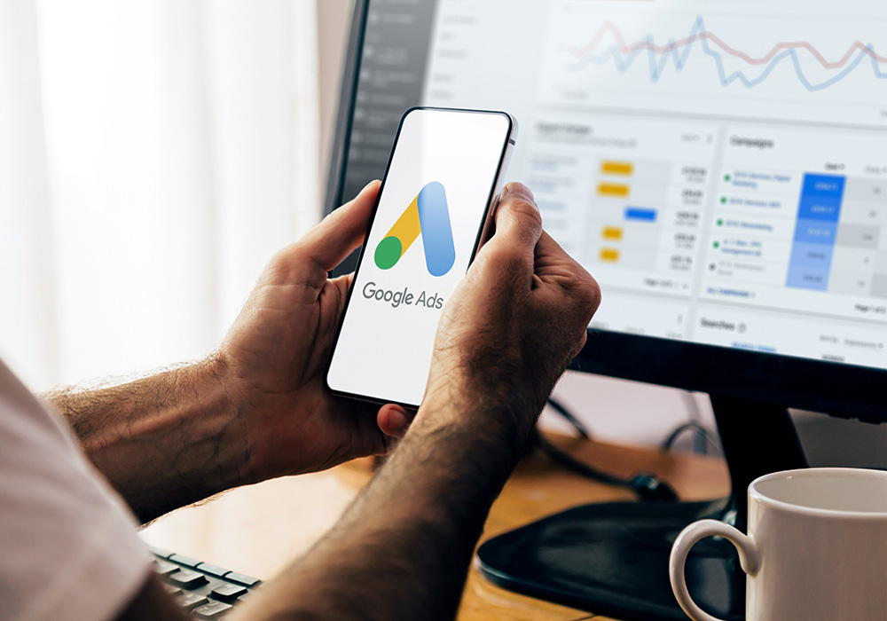 Google Ads logo on screen with computer in background with graphs on screen